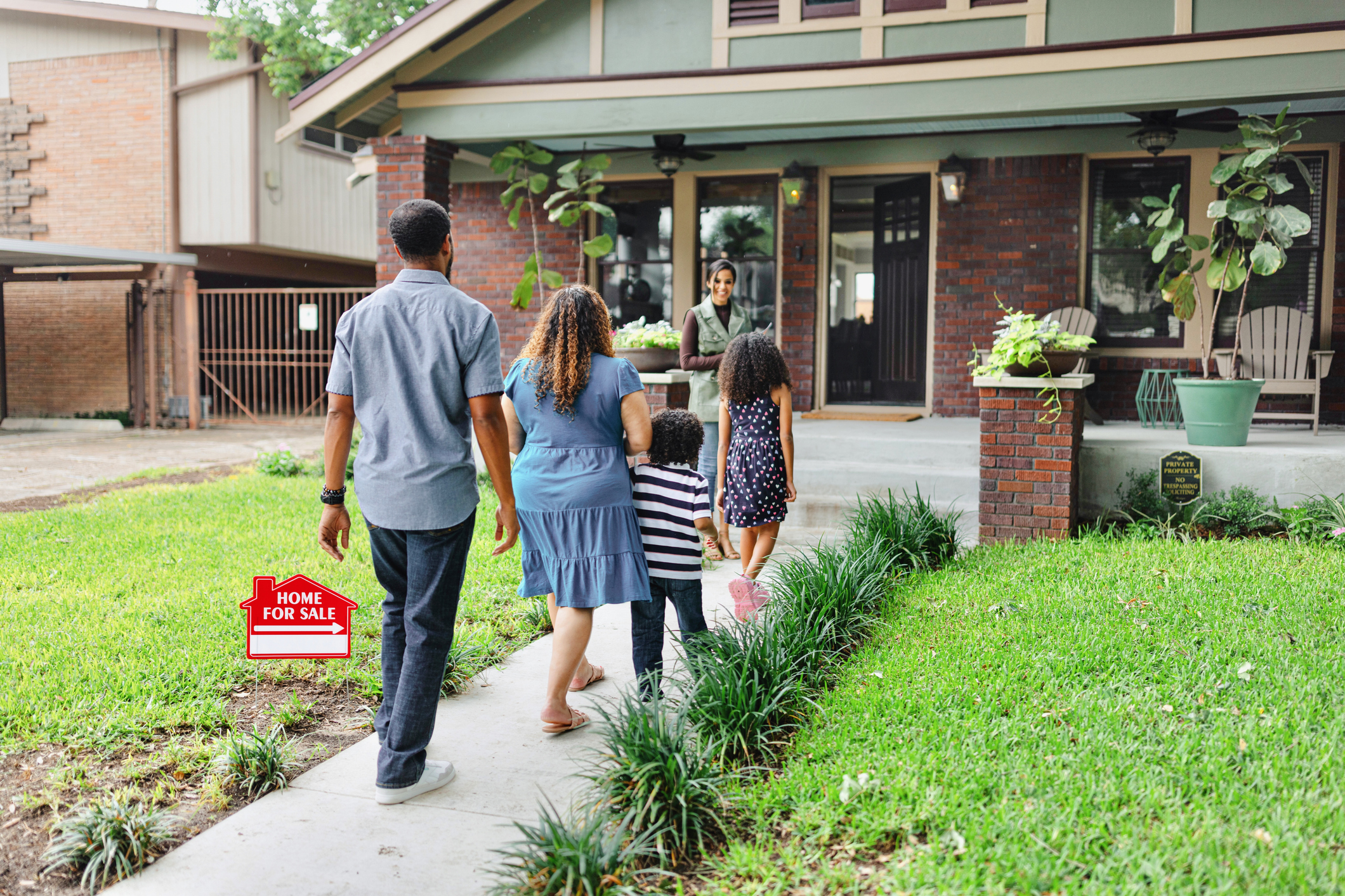 Family visiting house with "For Sale" sign.