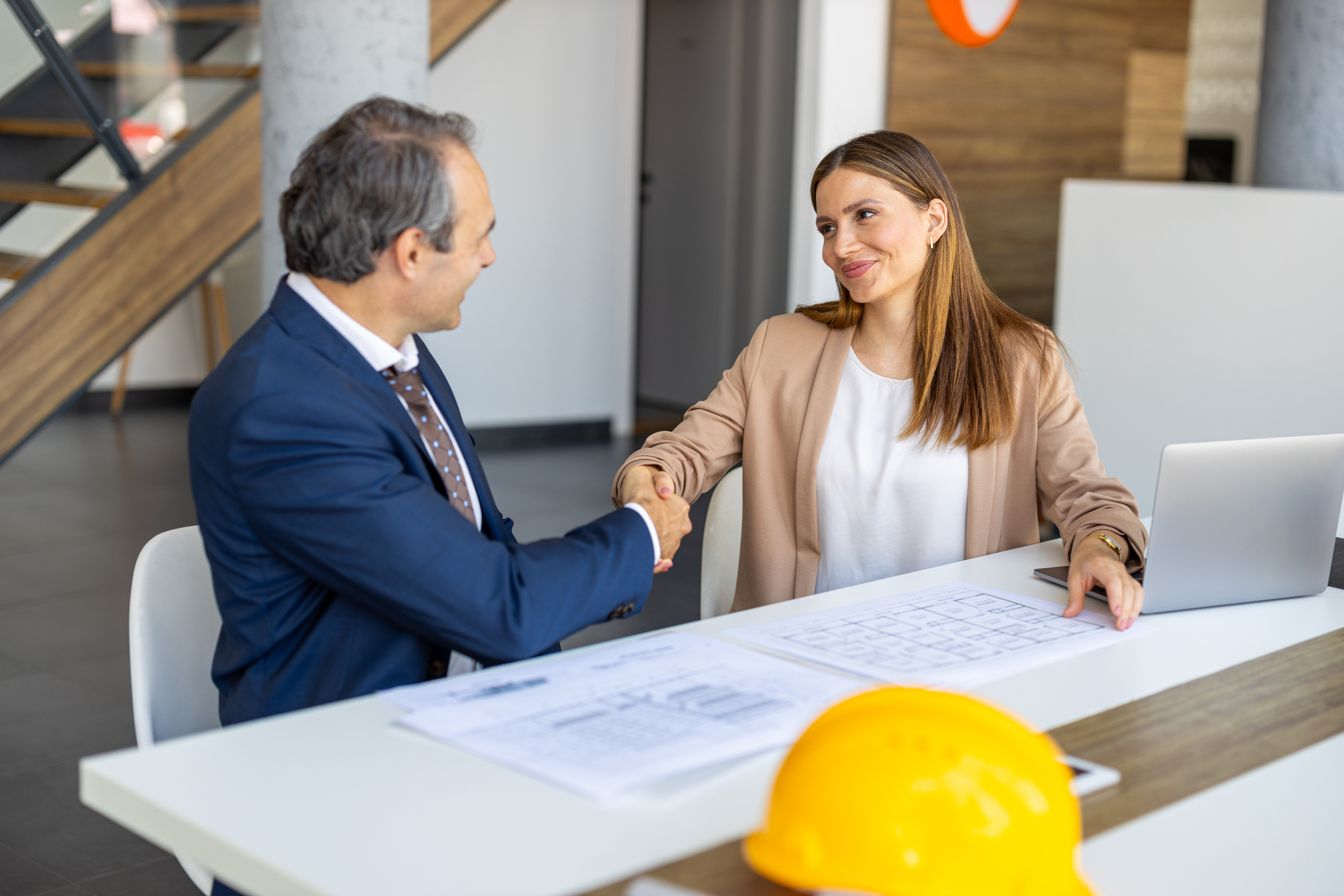 Two professionals shaking hands at desk.