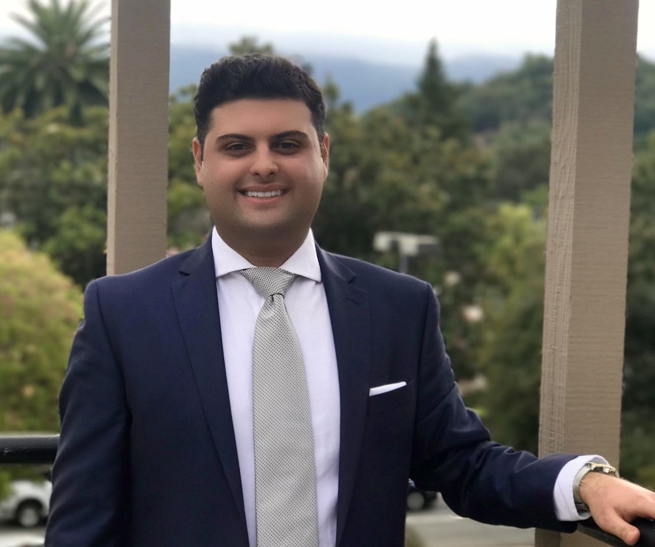 Man in suit smiling outdoors on balcony.