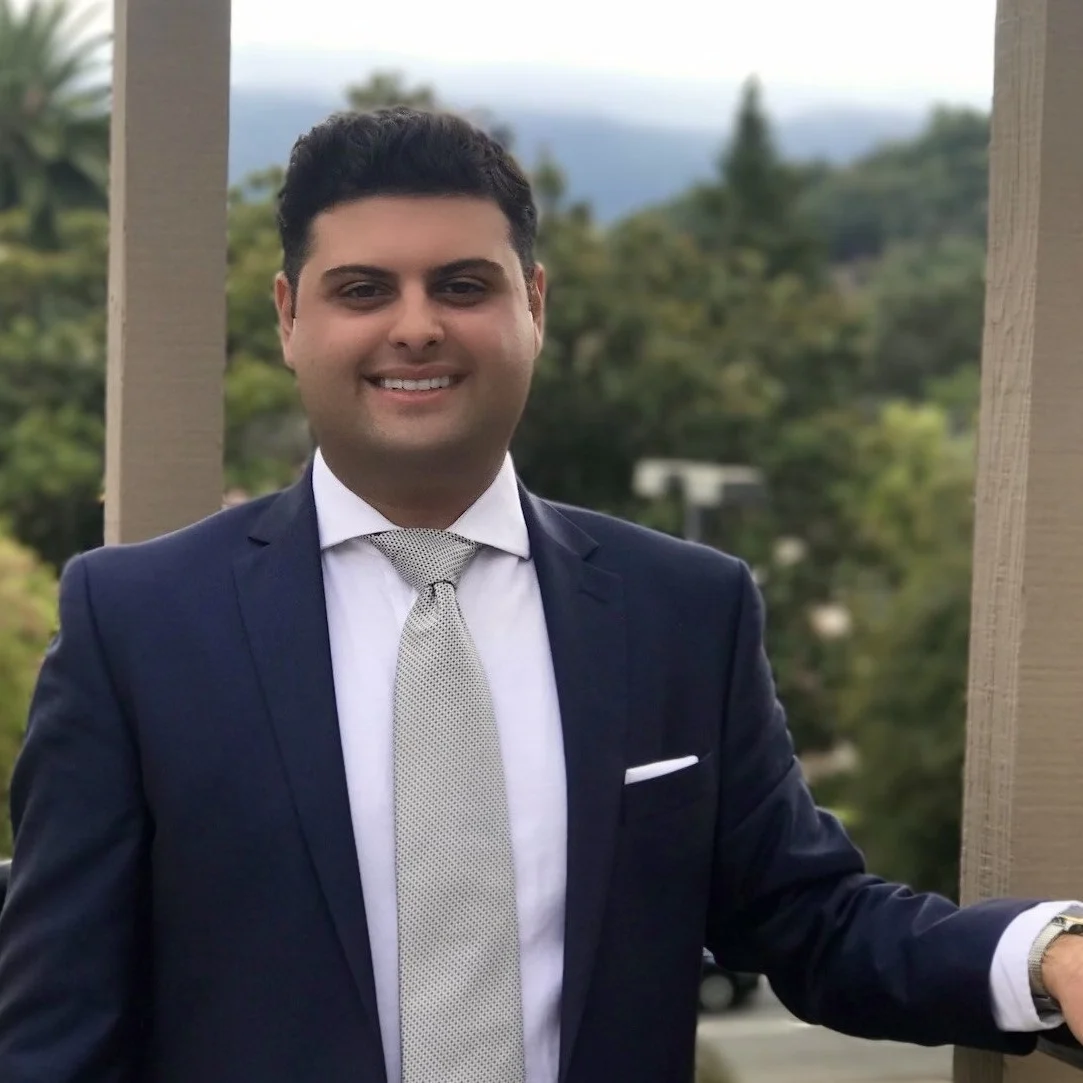 Man in suit smiling outdoors on balcony.